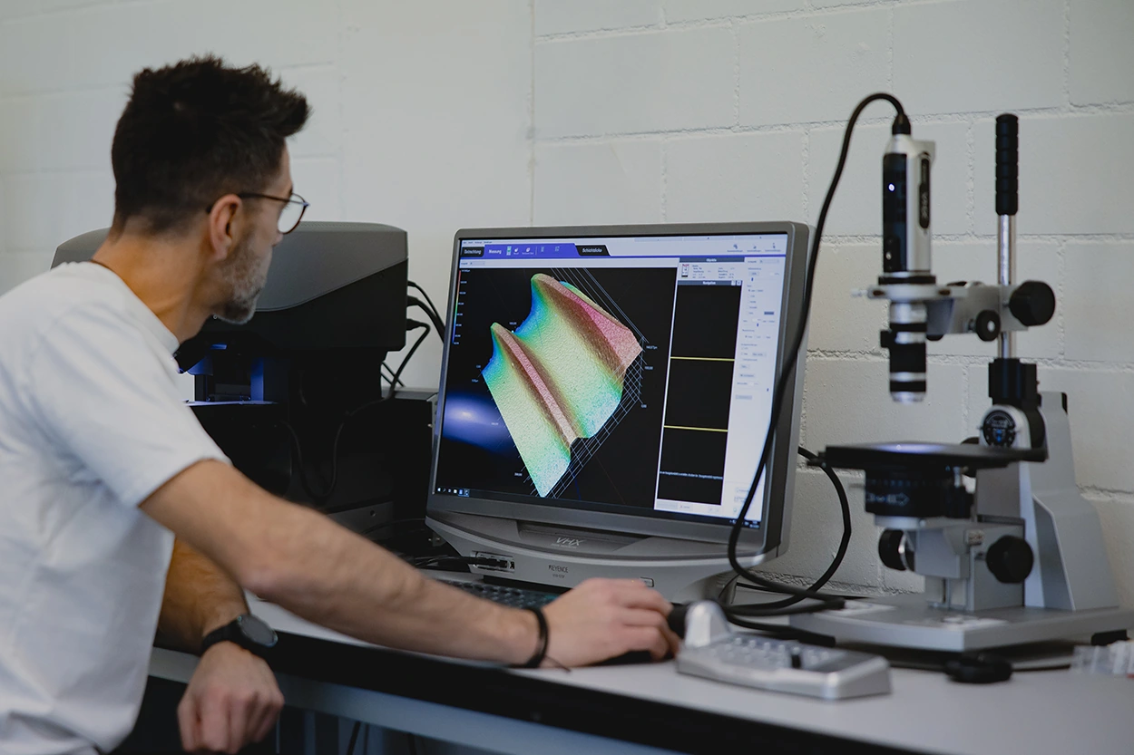 awalux Mitarbeiter begutachtet die Oberfläche eines Zahnimplantes unter auf einem Bildschirm neben einem Rasterelektronenmikroskop