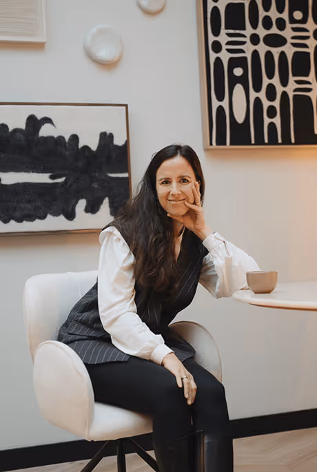 Yvonne Elzas, oprichter van De Legacy Video, zit ontspannen in een witte stoel voor abstracte kunst