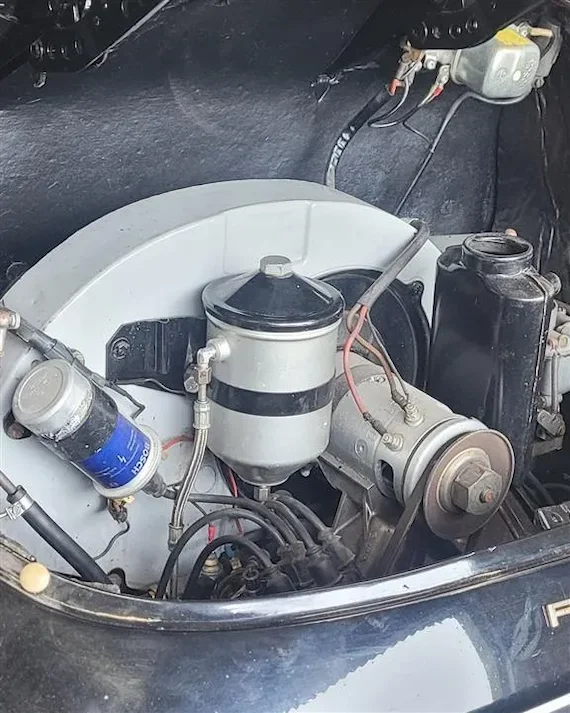 Close-up of a vintage Porsche car engine featuring a silver air filter, blue Bosch oil filter, and various engine components.