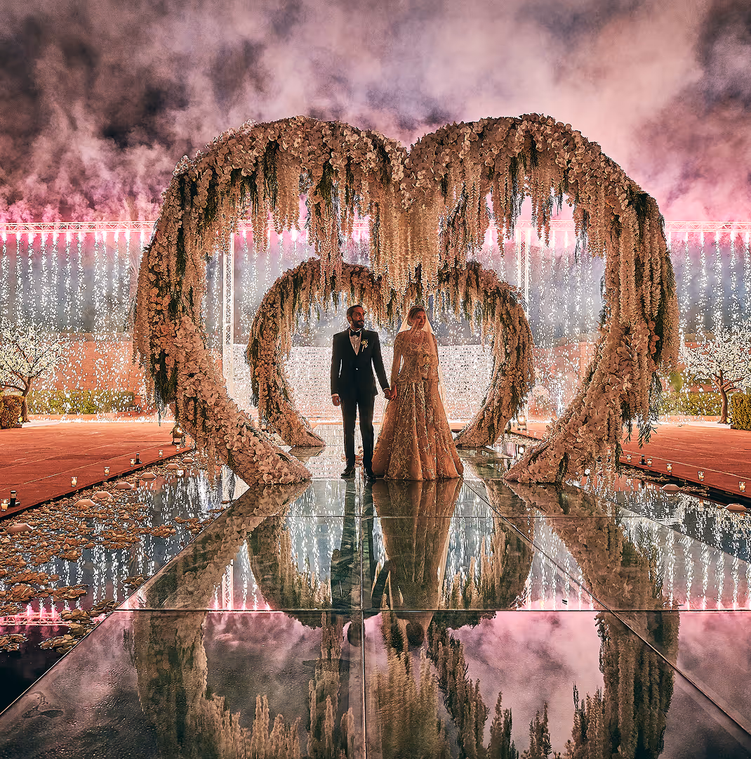 Outdoor wedding aisle lined with white floral arches and green grass under clear blue sky.