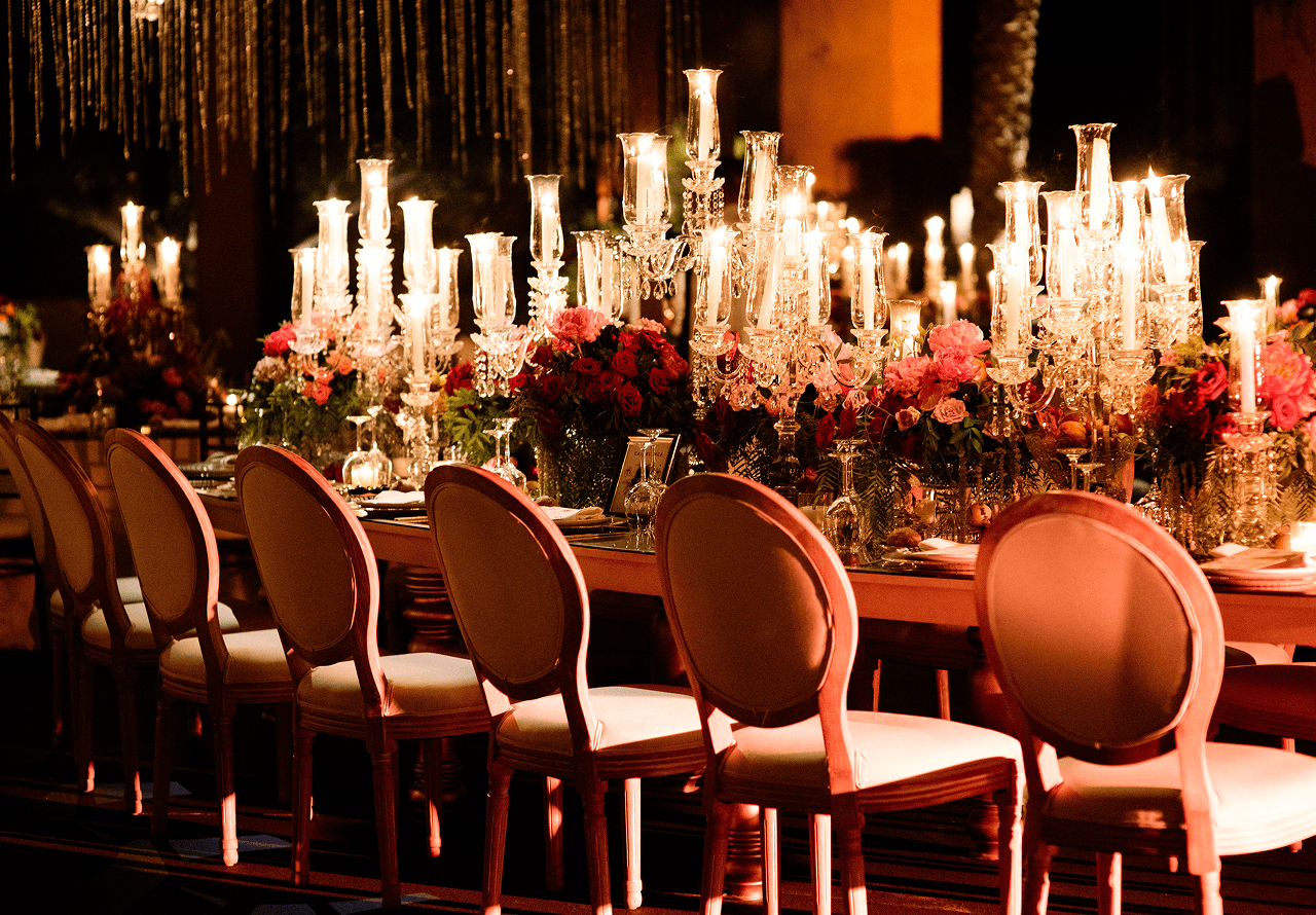 Elegant dining table with crystal candle holders, floral arrangements, and upholstered chairs in warm lighting.