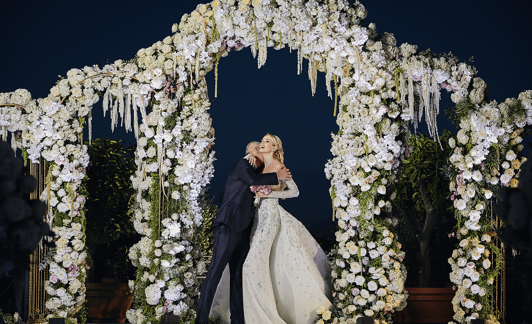 Sunlight shining through hanging white flowers and green leaves in an outdoor setting.