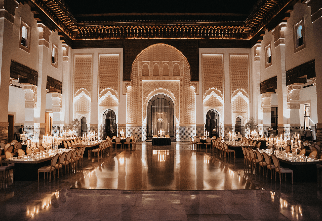 Lavishly decorated banquet hall with long tables, elegant chairs, and glowing candlelit chandeliers.