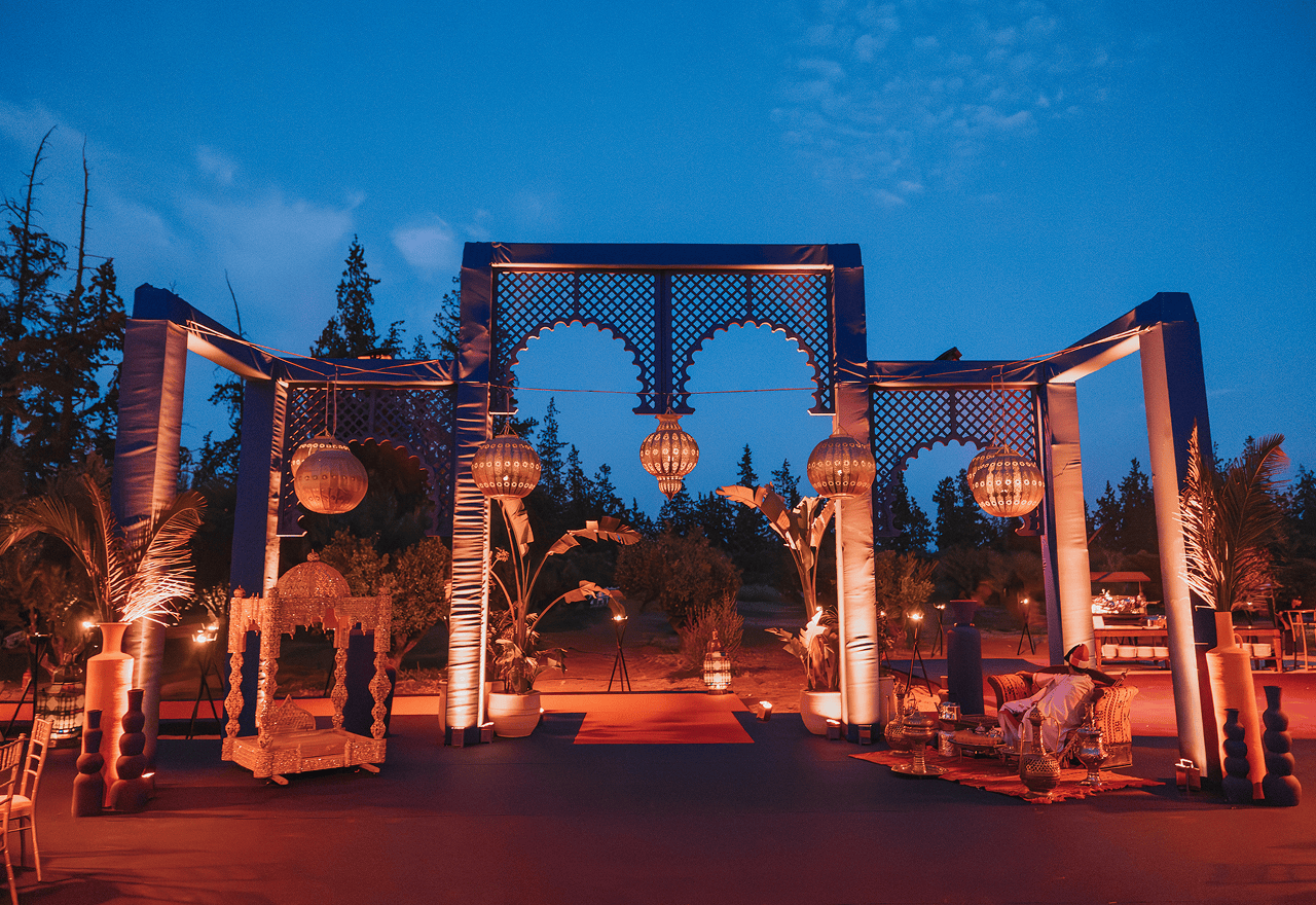 Outdoor decorative pavilion with hanging lanterns, potted plants, and ambient lighting at dusk.