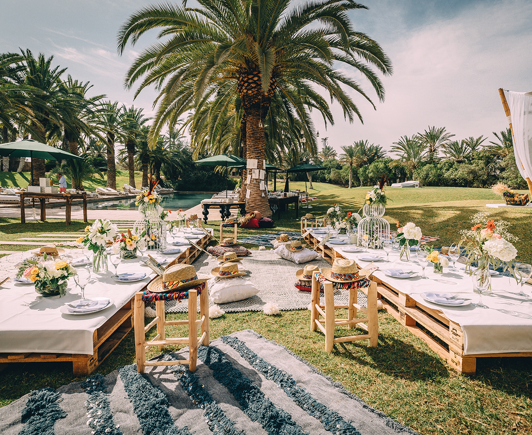 Bride and groom holding hands at an outdoor wedding altar adorned with abundant white flowers and surrounded by bridesmaids and groomsmen.