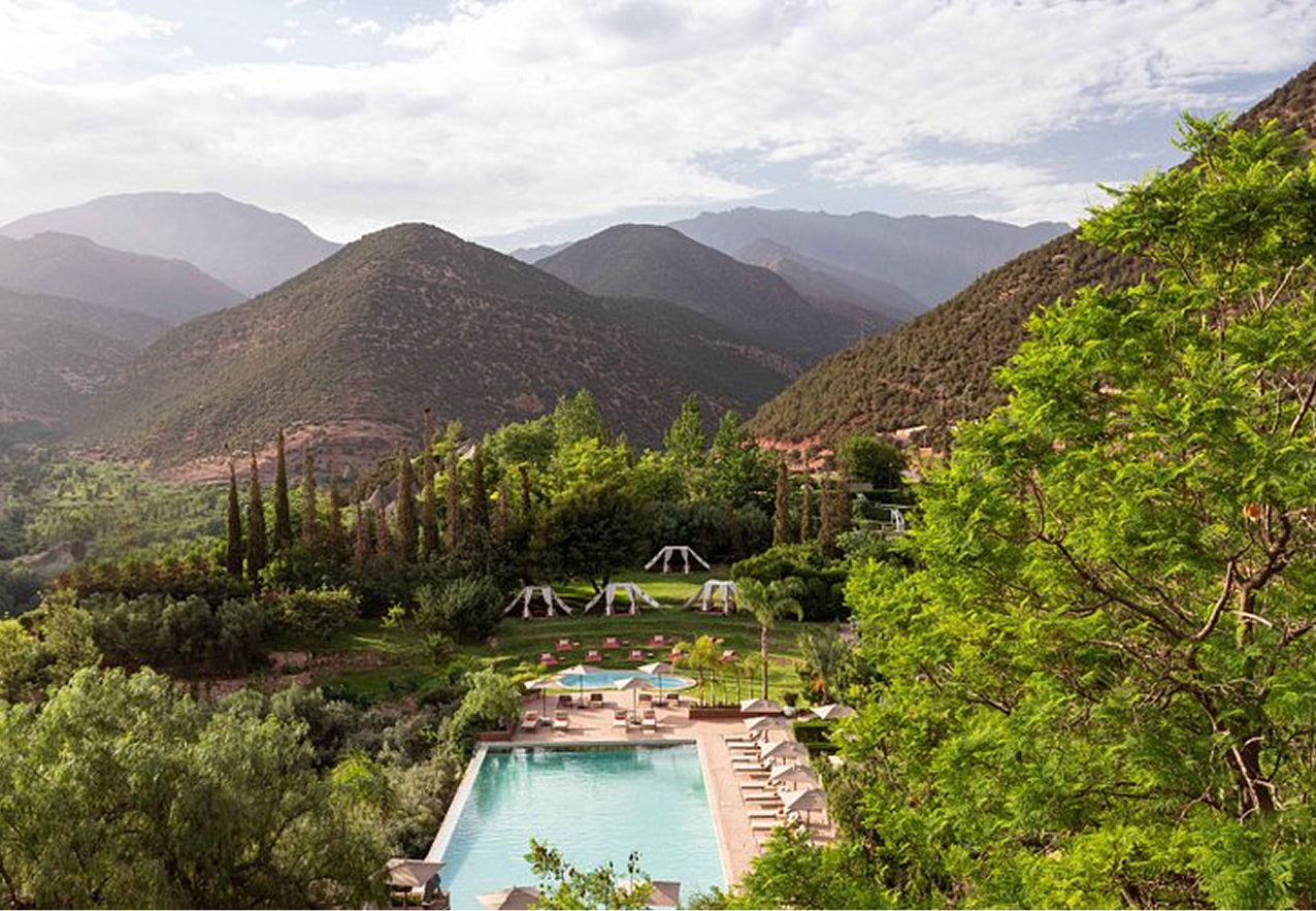 Elegant outdoor event with guests dining beside a large historic white building with ornate windows and greenery.