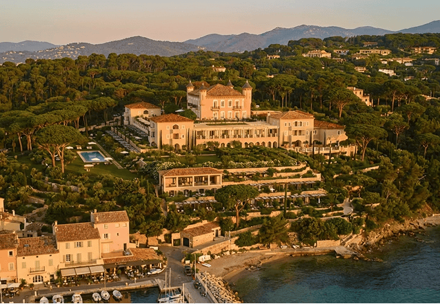 Elegant outdoor event with guests dining beside a large historic white building with ornate windows and greenery.