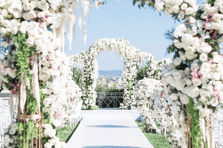 Long table set with white plates, crystal glasses, and decorated with lush green and white floral arrangements for an elegant event.