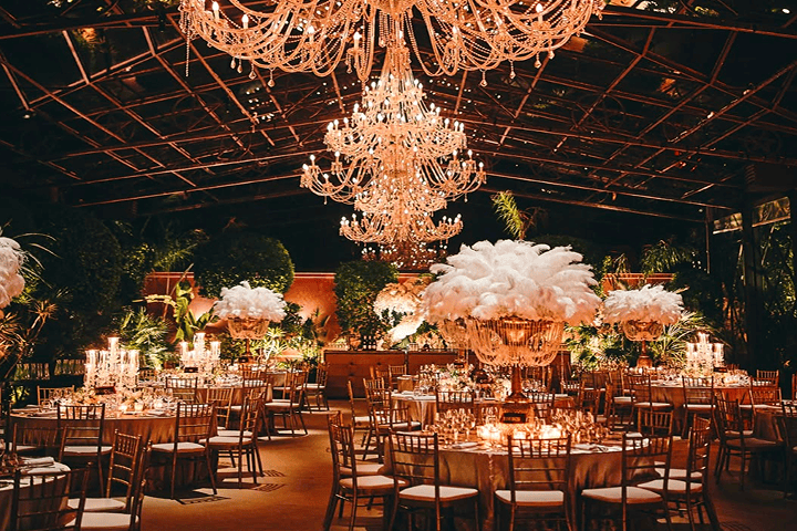 Outdoor wedding aisle decorated with white and pink floral arrangements and a flower-covered arch under a clear blue sky.