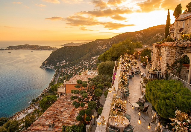 Elegant outdoor event with guests dining beside a large historic white building with ornate windows and greenery.