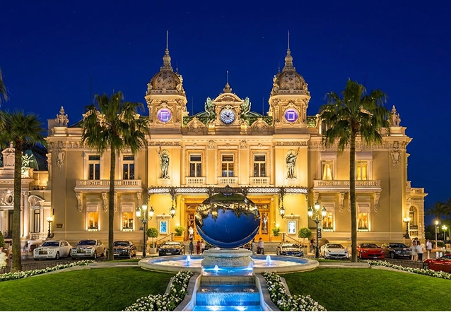 Elegant outdoor event with guests dining beside a large historic white building with ornate windows and greenery.
