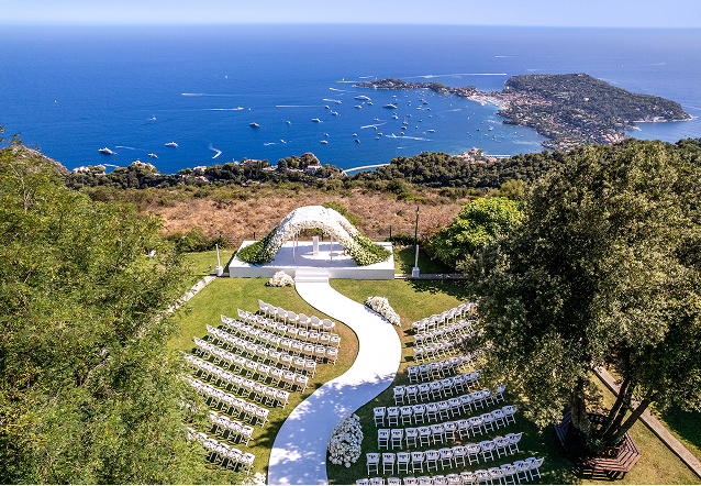 Elegant outdoor event with guests dining beside a large historic white building with ornate windows and greenery.
