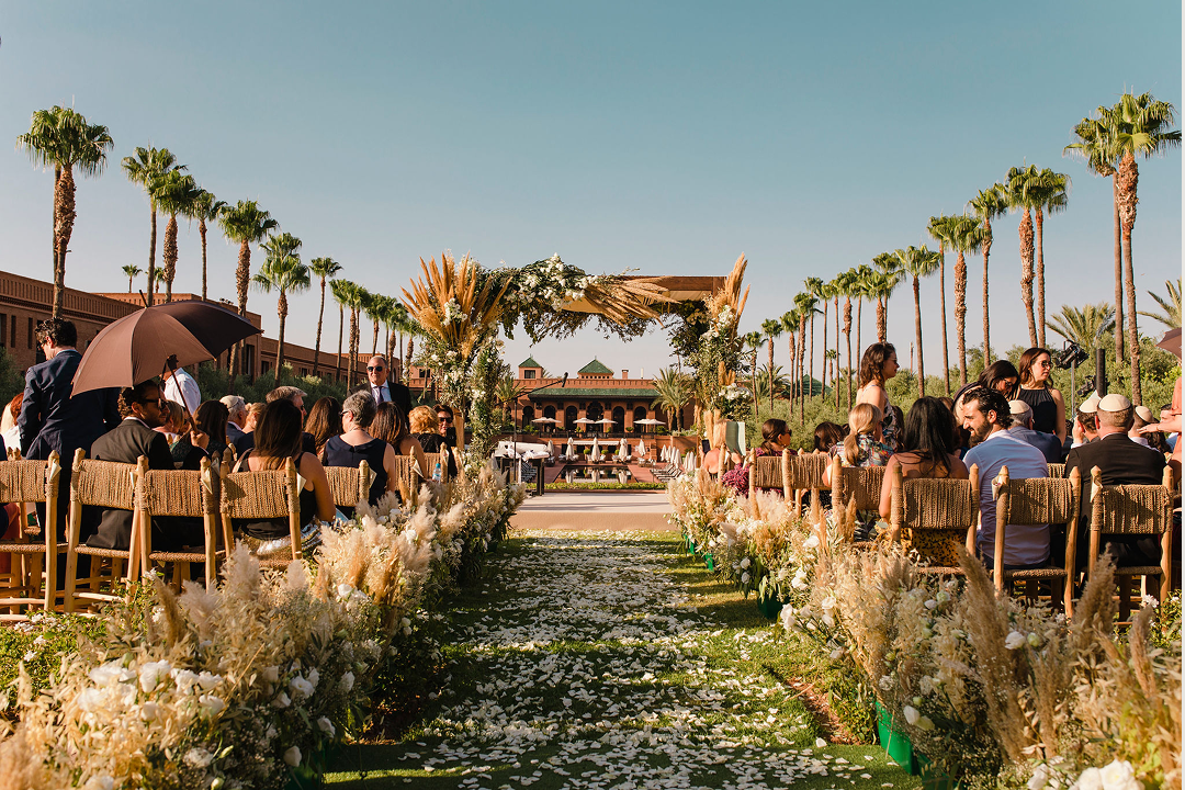 Long table set with white plates, crystal glasses, and decorated with lush green and white floral arrangements for an elegant event.