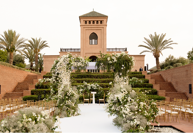 Elegant outdoor event with guests dining beside a large historic white building with ornate windows and greenery.
