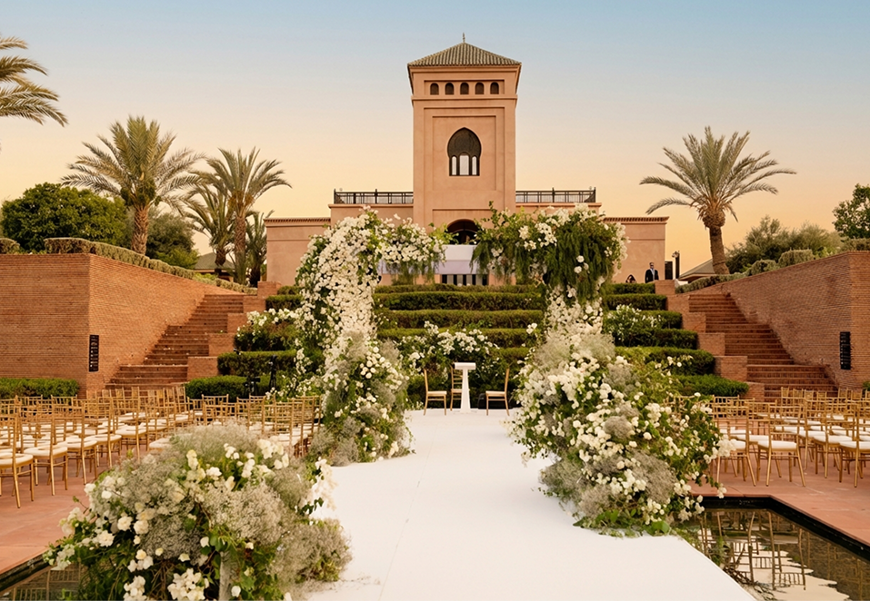 Elegant outdoor event with guests dining beside a large historic white building with ornate windows and greenery.