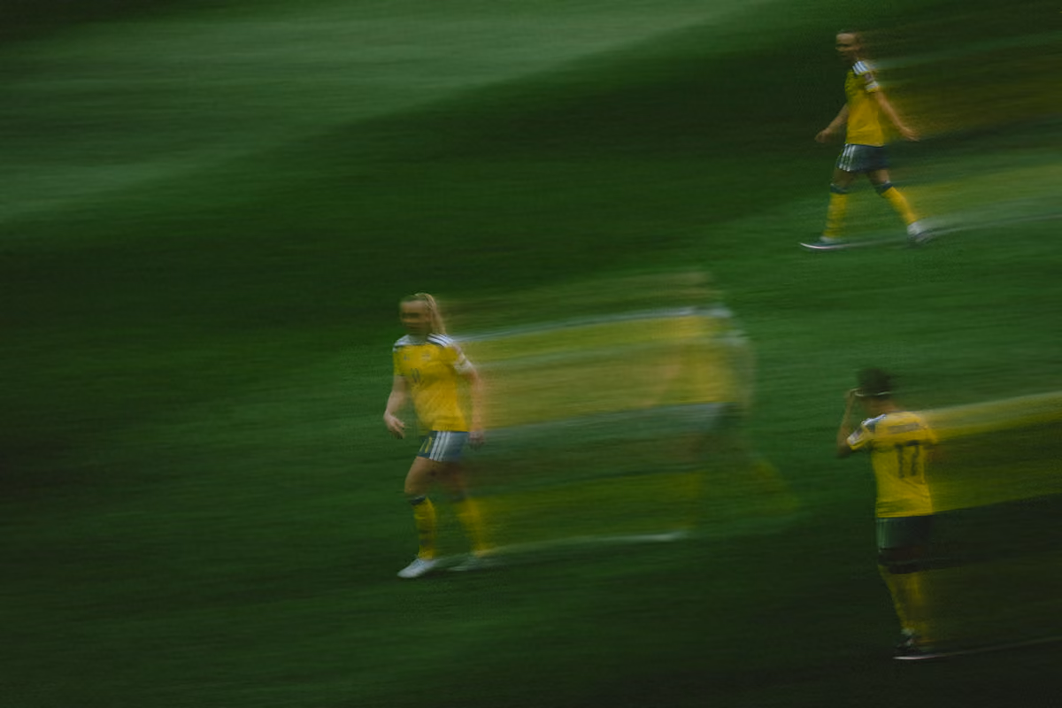 Suddayta bild av fyra fotbollsspelare i gula tröjor på en grön gräsmatta med rörelseoskärpa som skapar en effekt av flera halvbilder omkring dem.