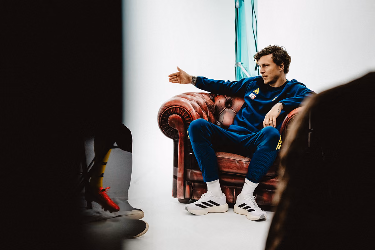 Man in blue sportswear sitting on a red leather armchair with one arm extended, white background, casual setting.