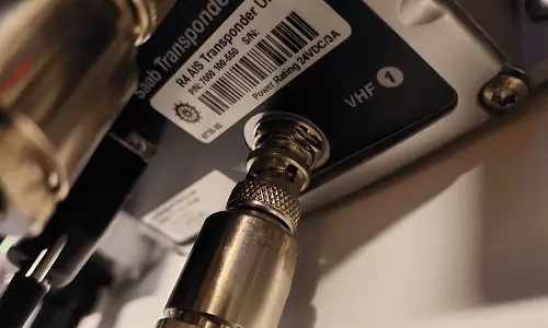 Close-up of a metal coaxial cable connector plugged into a device labeled 'RAI AS Transponder' and 'VHF 1'.