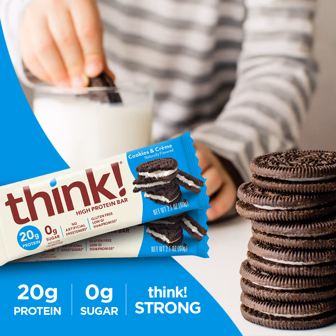 Stack of chocolate sandwich cookies next to Think! high protein bar with cookies and cream flavor, and a person dipping a cookie in a glass of milk.
