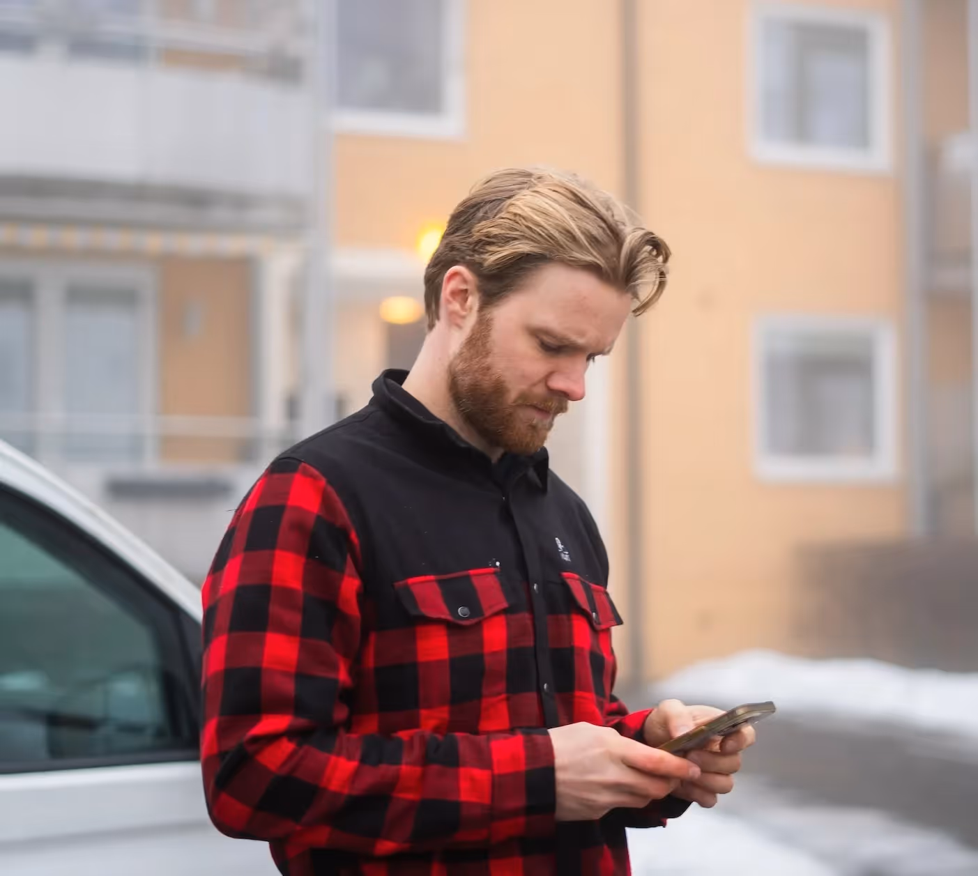 Mann ute i rødt og svart rutemønster skjorte ser på mobilen sin.