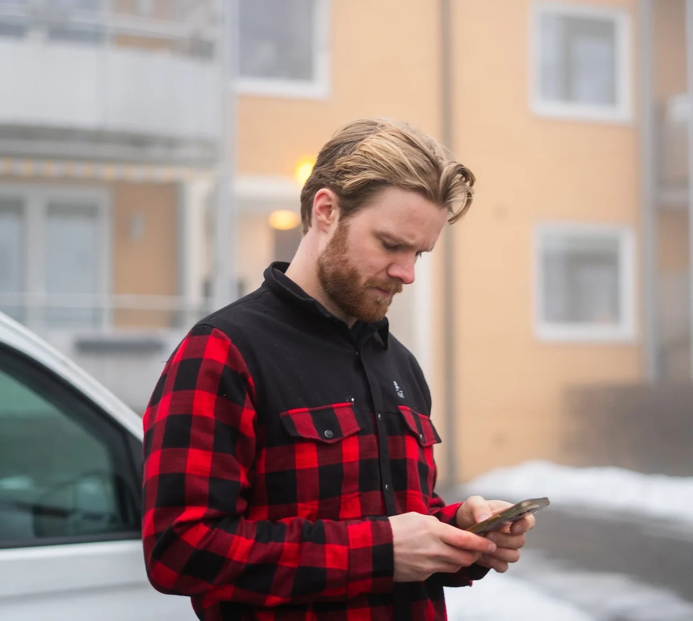 Mann ute i rødt og svart rutemønster skjorte ser på mobilen sin.