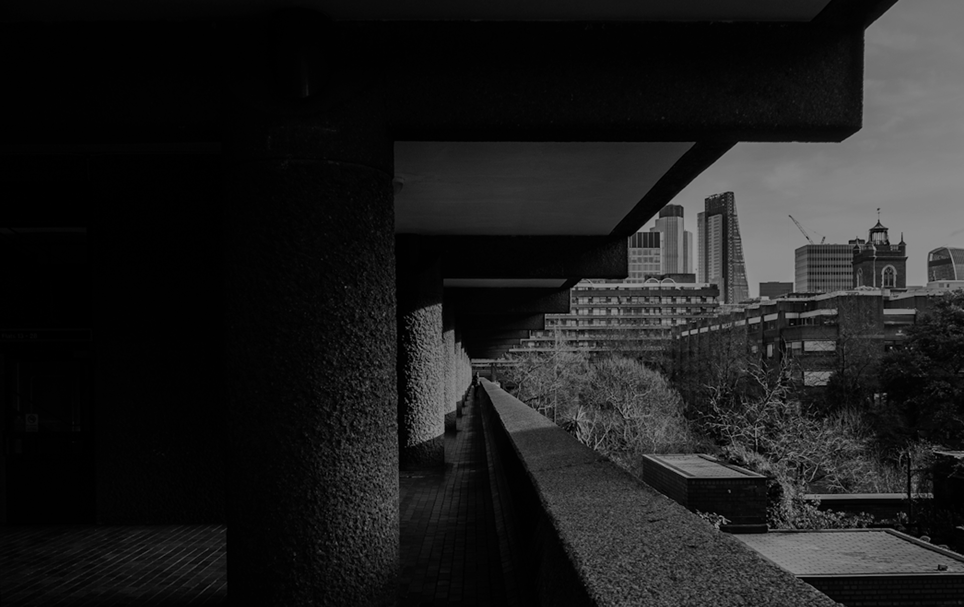 A photo of the barbican looking along a walkway with greenary to one side. Black and white