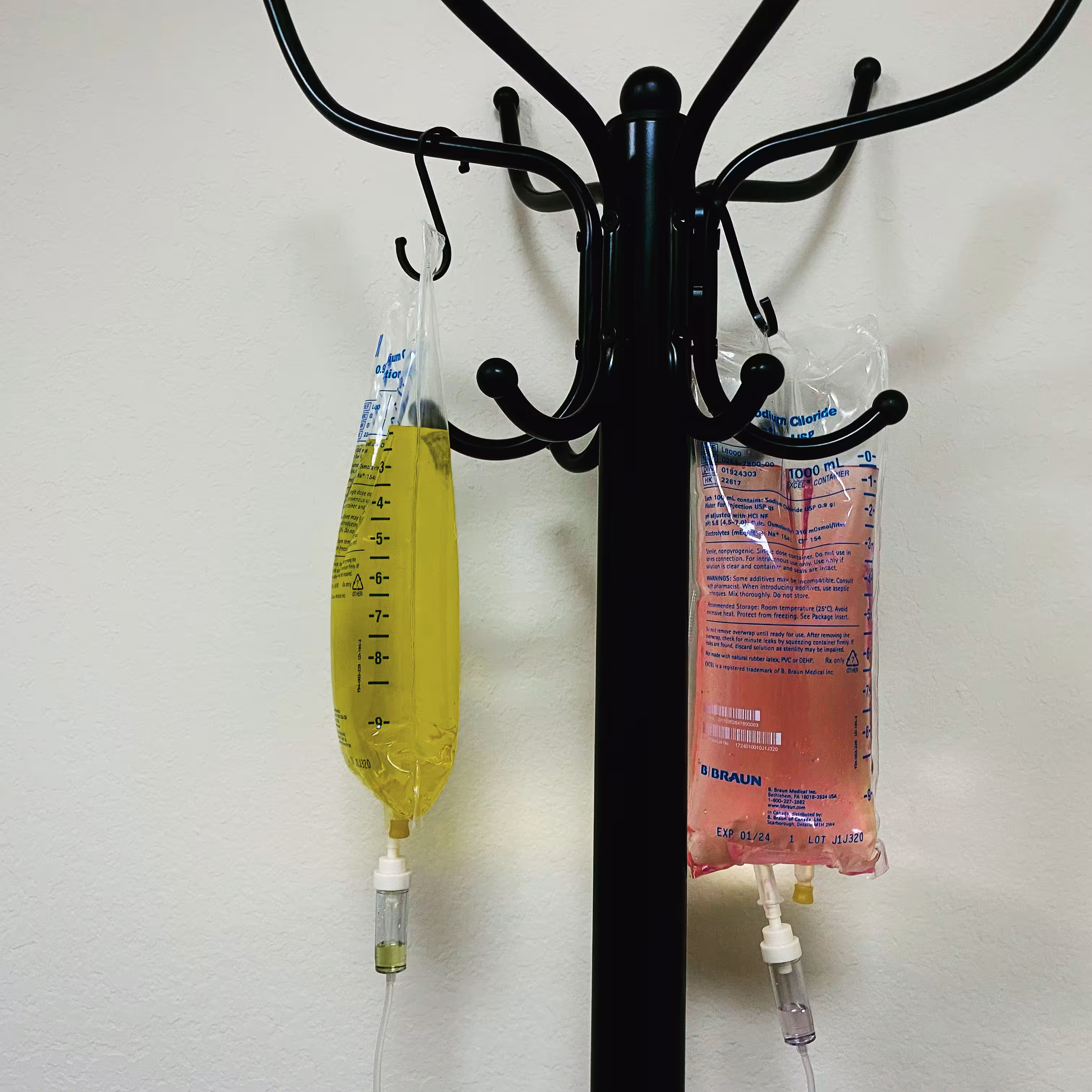Two IV bags hanging on a black metal stand, one filled with yellow liquid and the other with pink liquid.