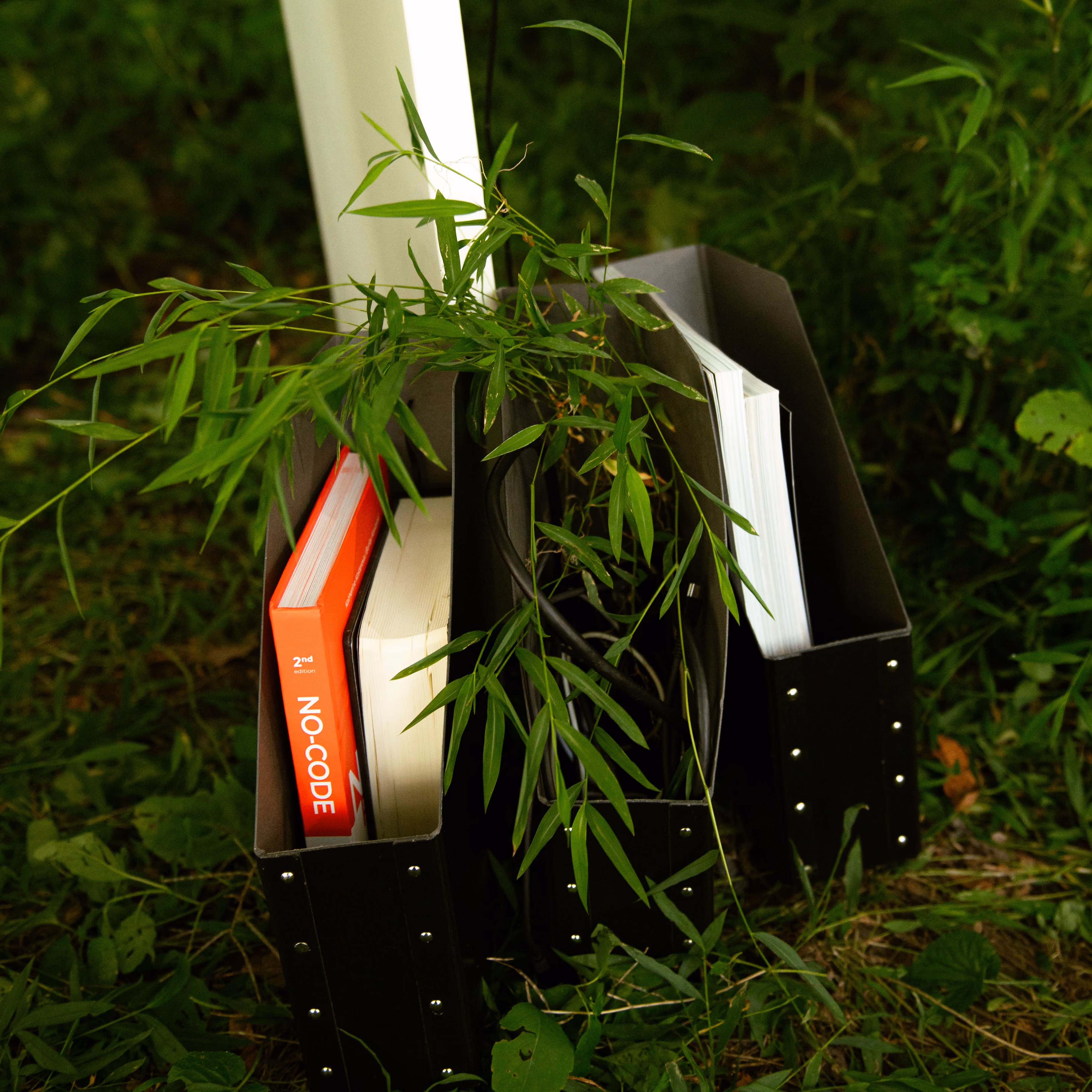 Black file organizers holding books and folders, tucked in the grass beside a white desk