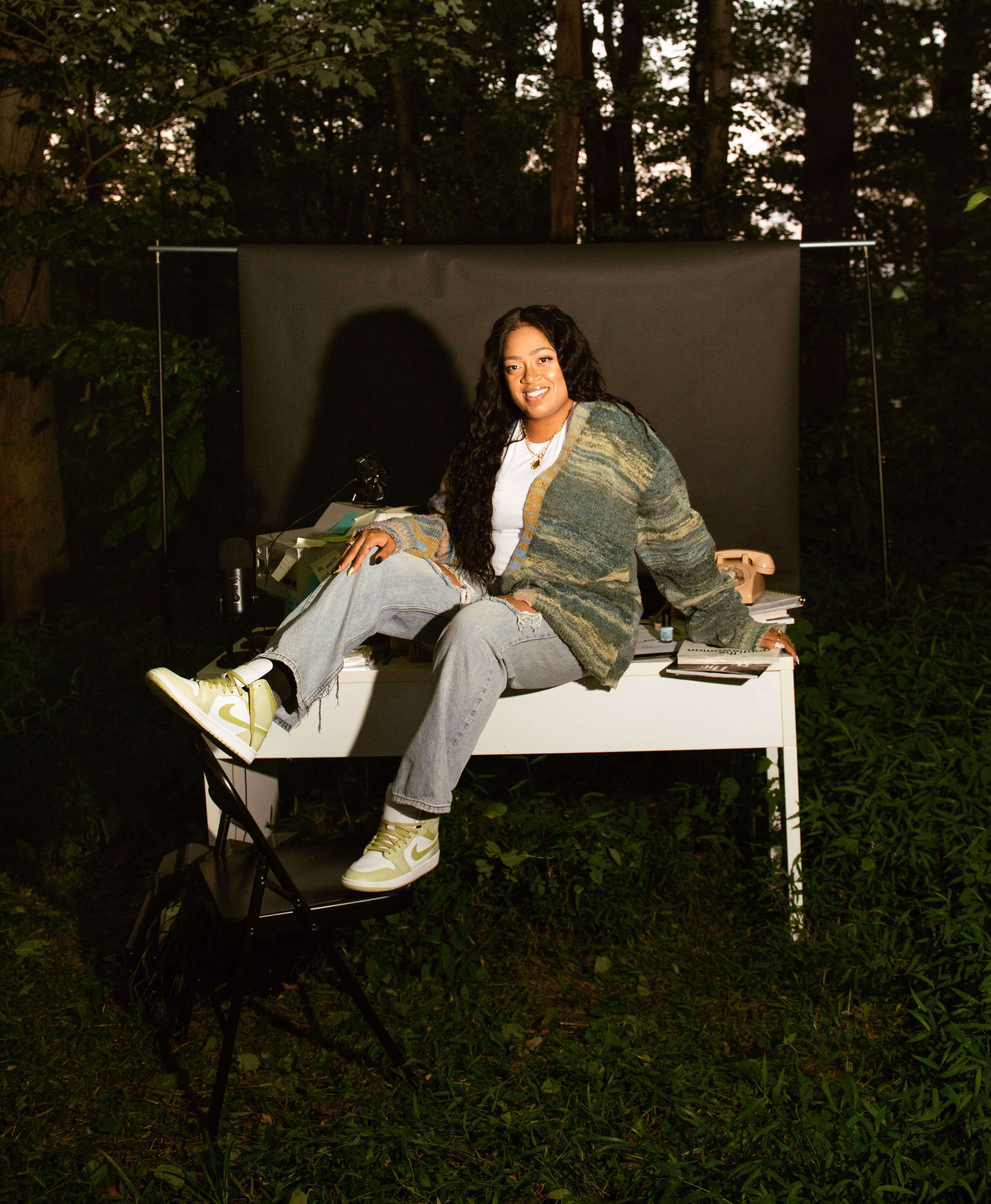 Domanique Taylor, a Black website designer in Pittsburgh, sitting on a white desk at an outdoor photoshoot
