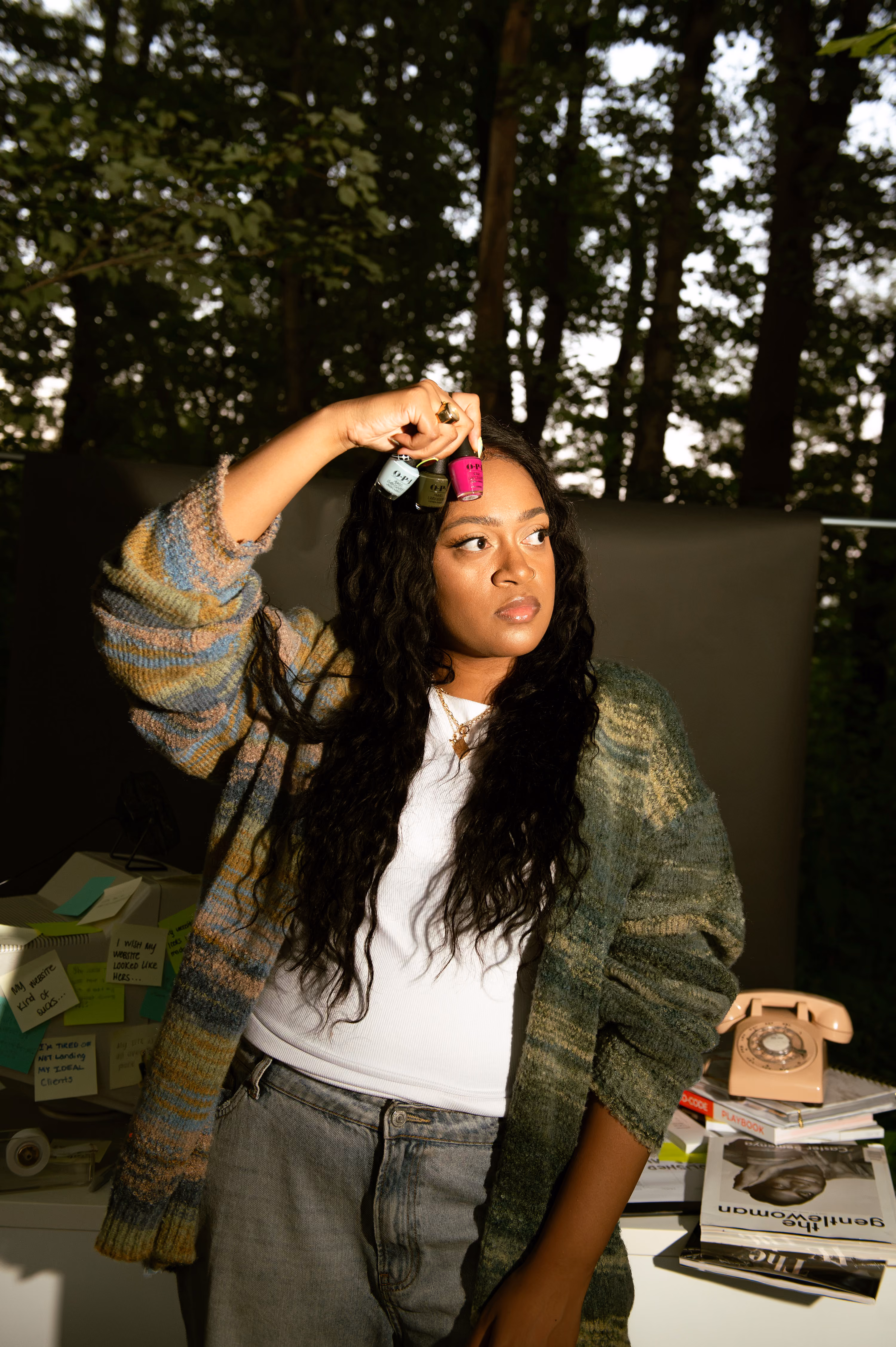 Website strategist Domanique Taylor holding up bottles of nail polish at her outdoor desk