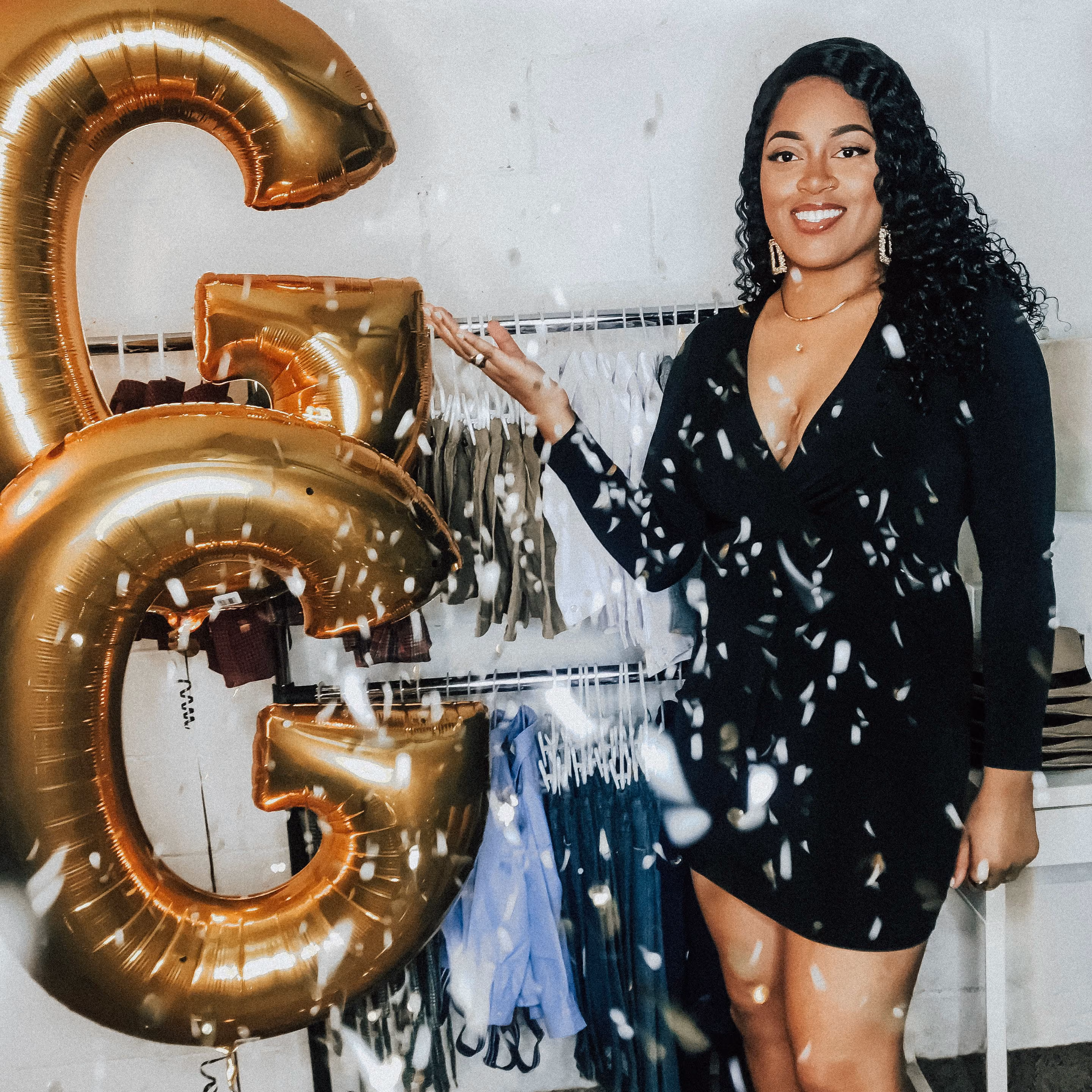 Domanique Taylor posing next to giant gold letter balloons and a rack of kids' clothes for her boutique, Giggling Gentleman