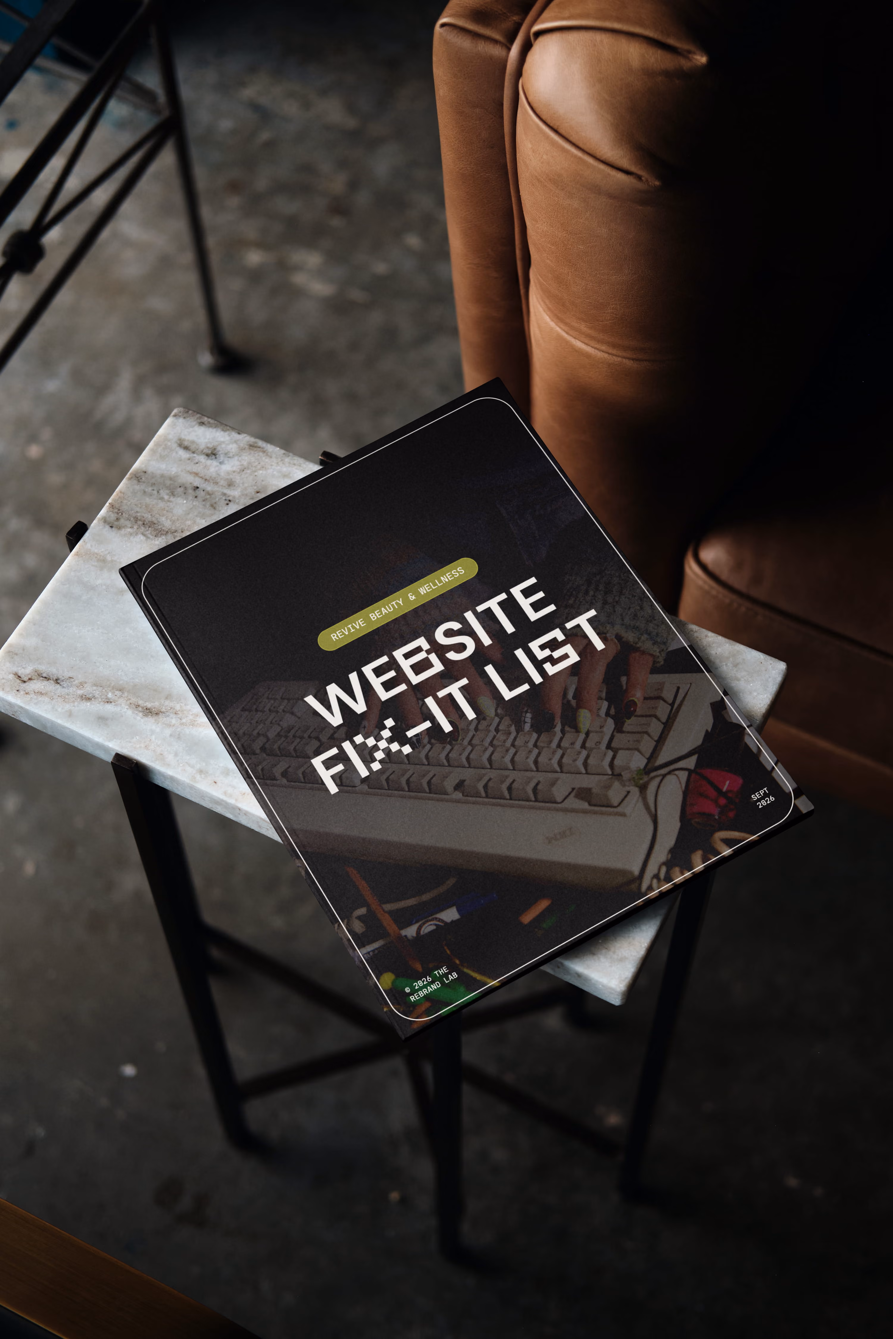 A 'Website Fix-It List' from a Polished Pages Audit with a subtitle 'Revive Beauty & Wellness' resting on a small marble table beside a brown leather chair.