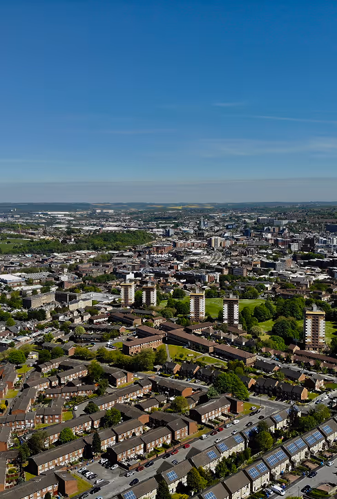 Aerial view of a city with residential houses, apartment buildings, green spaces, and a clear blue sky.
