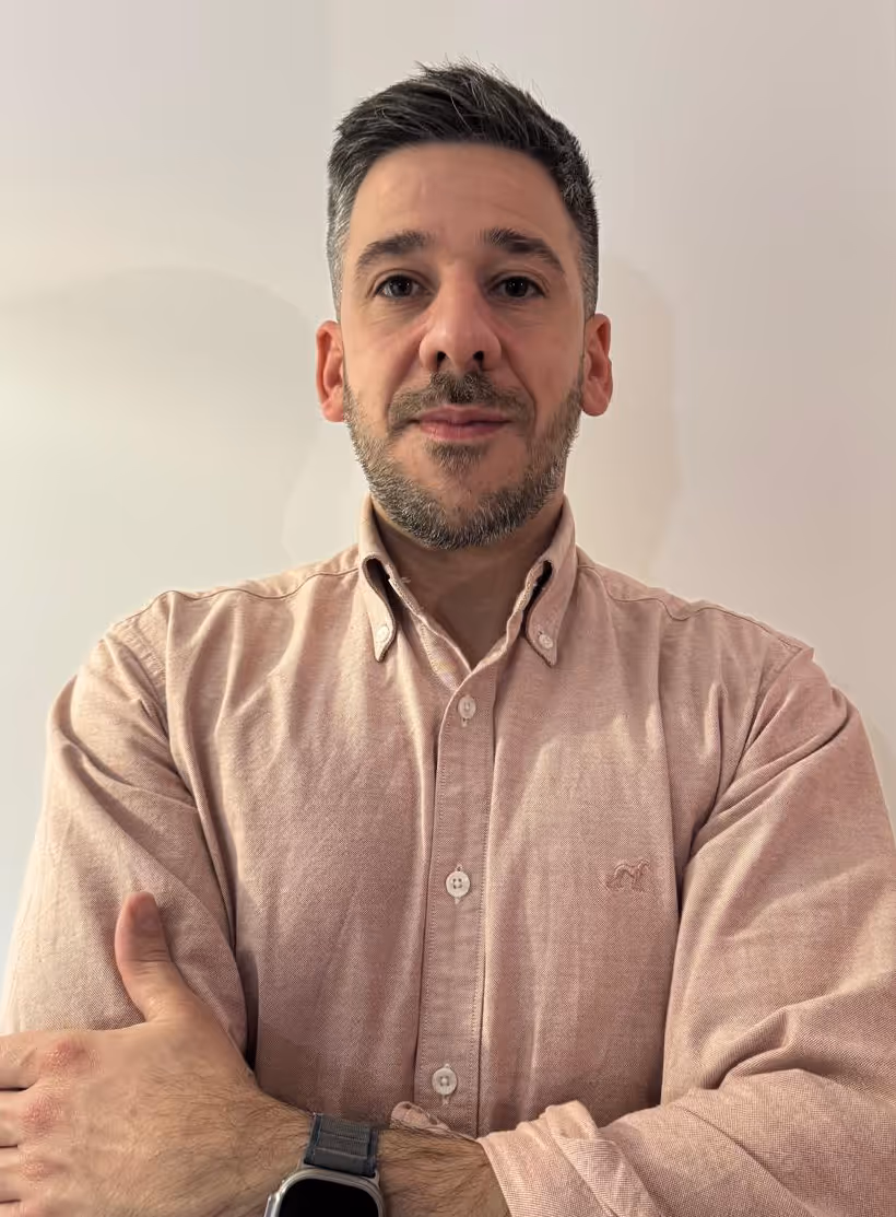 Homem de cabelo curto e barba curta viste uma camisa rosa claro com os braços cruzados e usa um relógio inteligente.