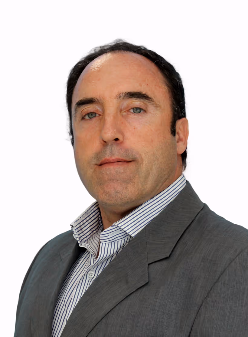 Homem de meia-idade com cabelo castanho escuro, camisa riscada branca e cinzenta e fato cinzento, olhando diretamente para a câmara.