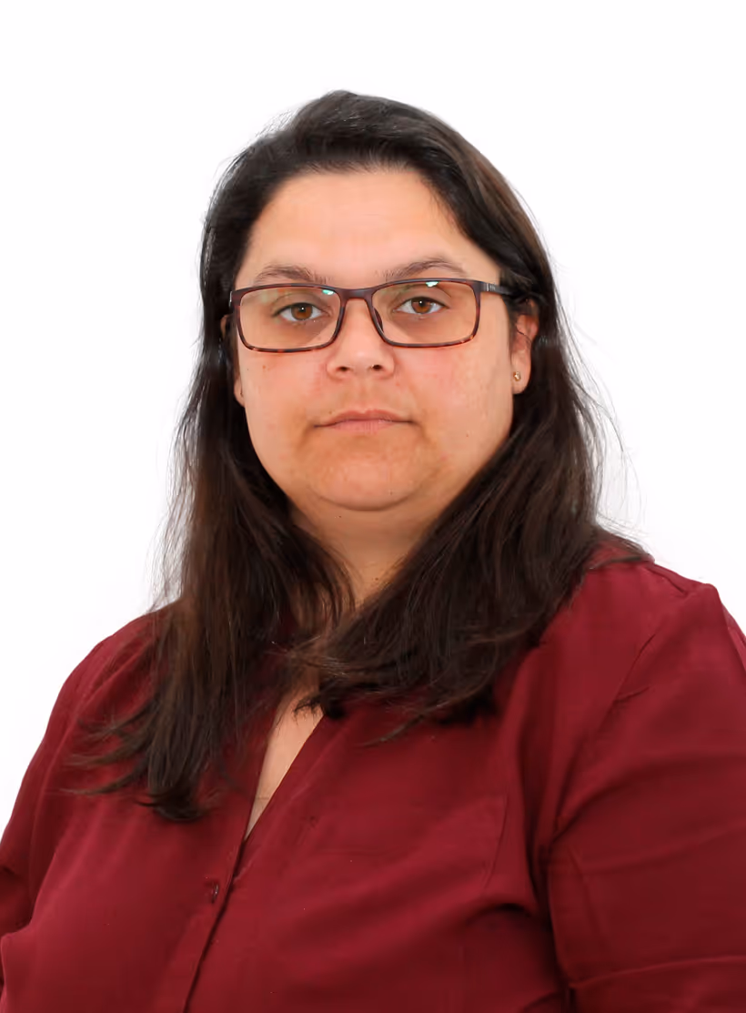 Mulher com cabelo castanho escuro e óculos castanhos, vestindo camisa vermelha, olhando para a câmara com fundo branco.