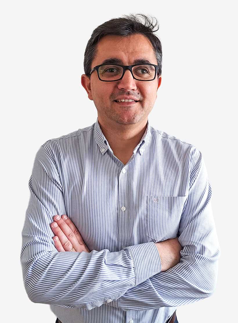 Homem de cabelo preto e óculos pretos, de camisa às riscas azul e branca, com os braços cruzados e rosto sorridente.