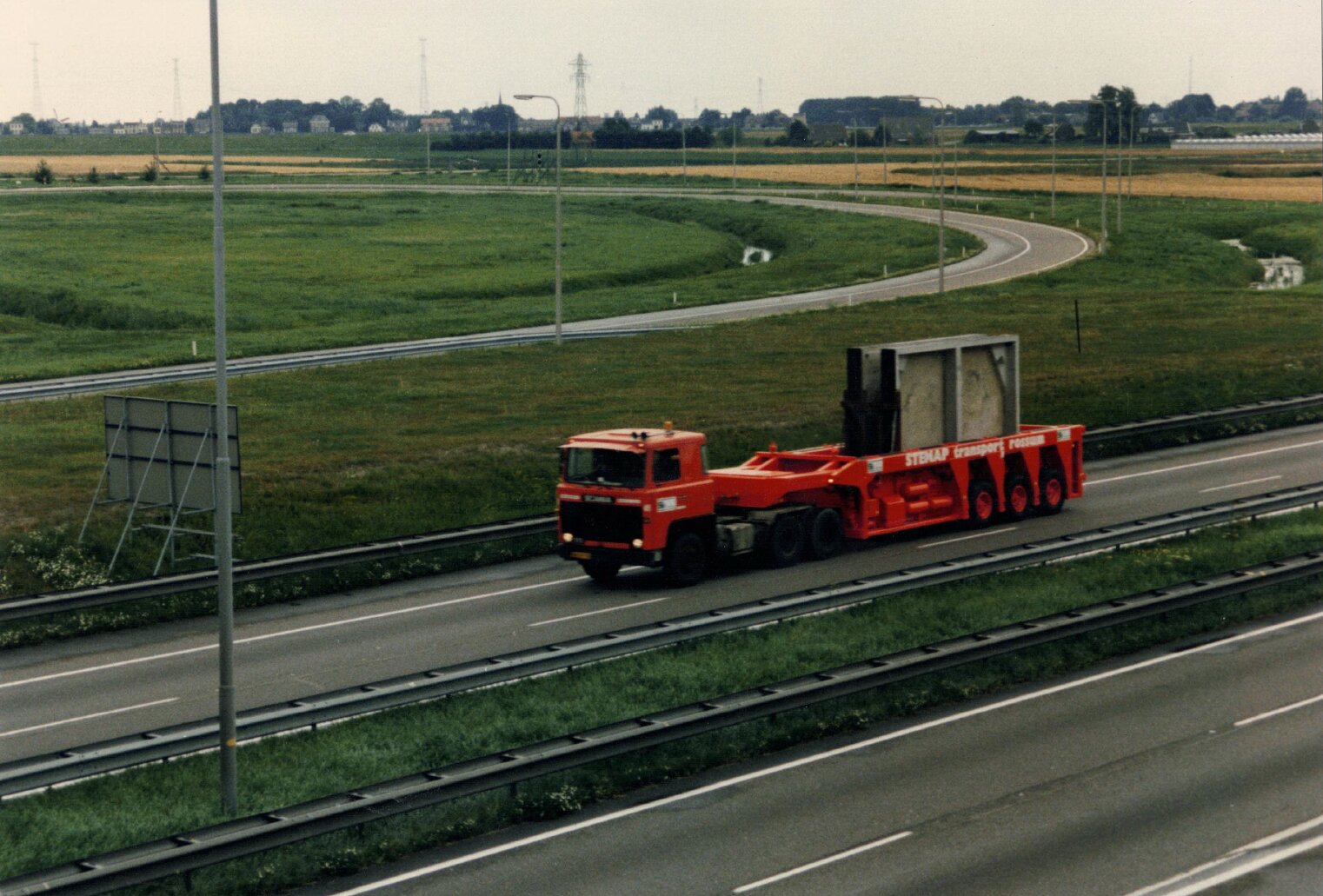 Historische foto circa jaren '90: Stenap vrachtwagen met lage trailer transporteert een grote betonnen constructie over een snelweg.