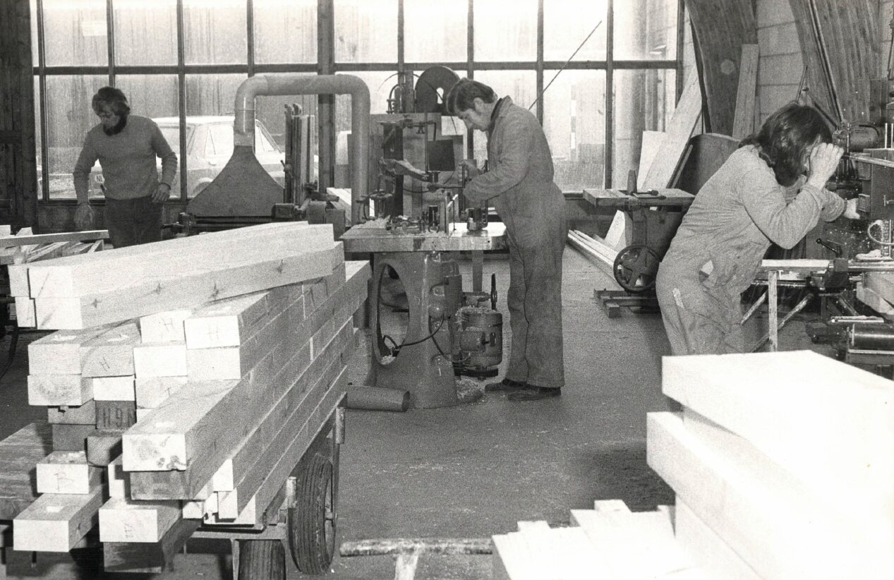 Historische foto circa jaren '60: arbeiders in een houtbewerkingswerkplaats met machines en houten balken.