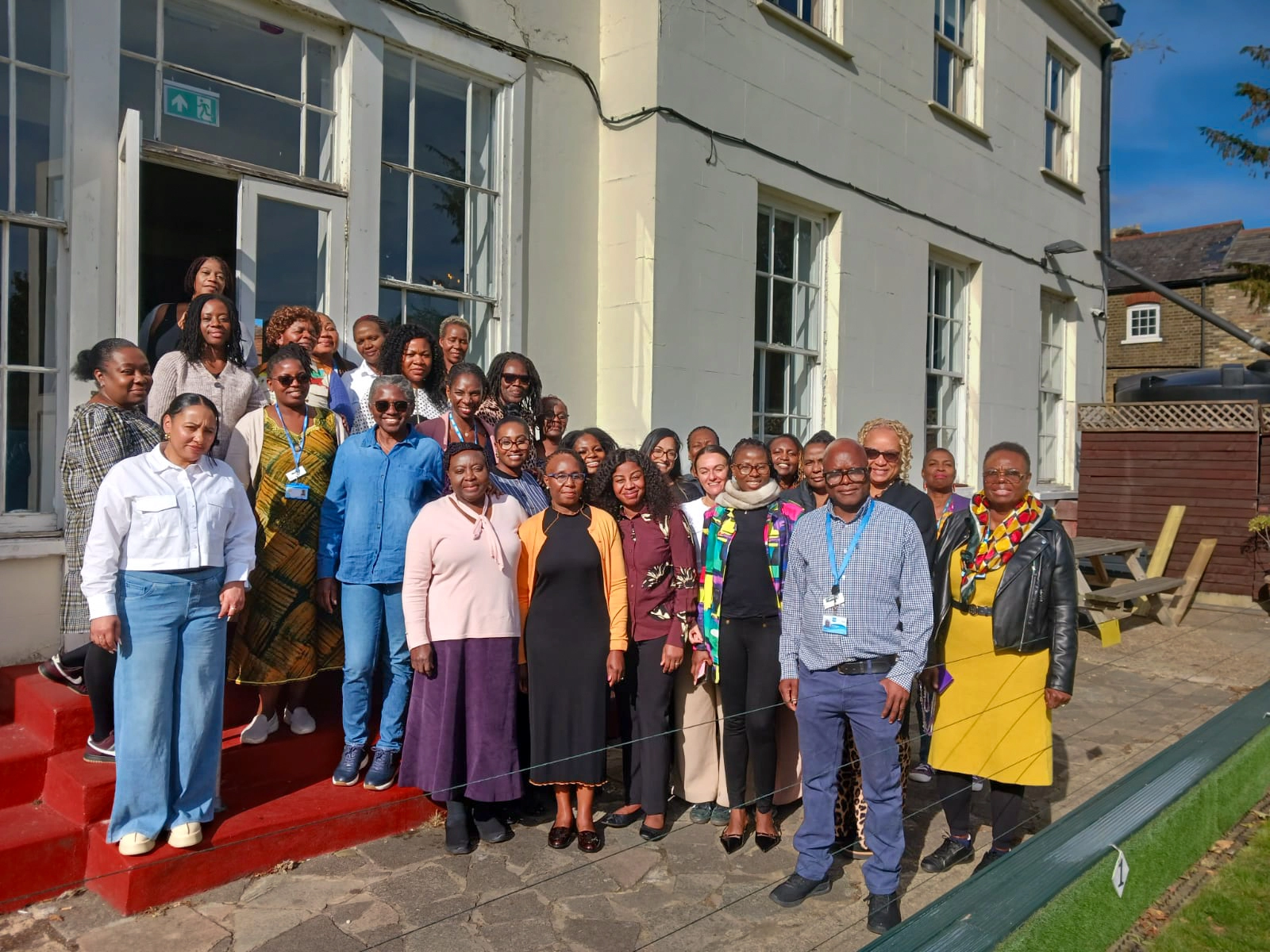 Group of diverse adults standing together outdoors in front of a building with large windows on a sunny day.