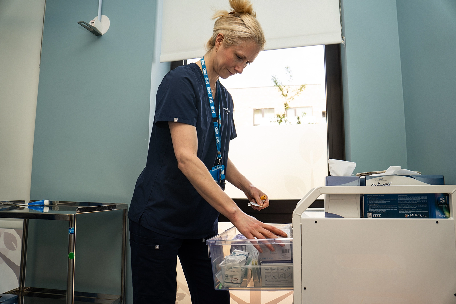 Nurse in navy scrubs organising medical supplies in a drawer inside a medical room.