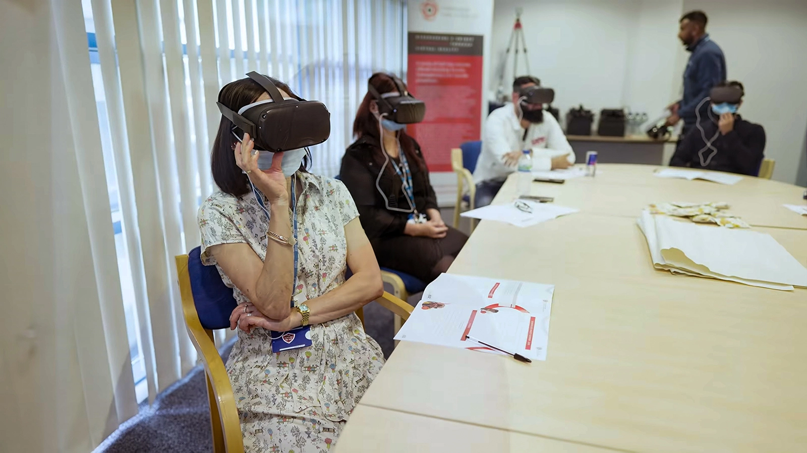 Group of people seated around a conference table wearing VR headsets and face masks during a training session.