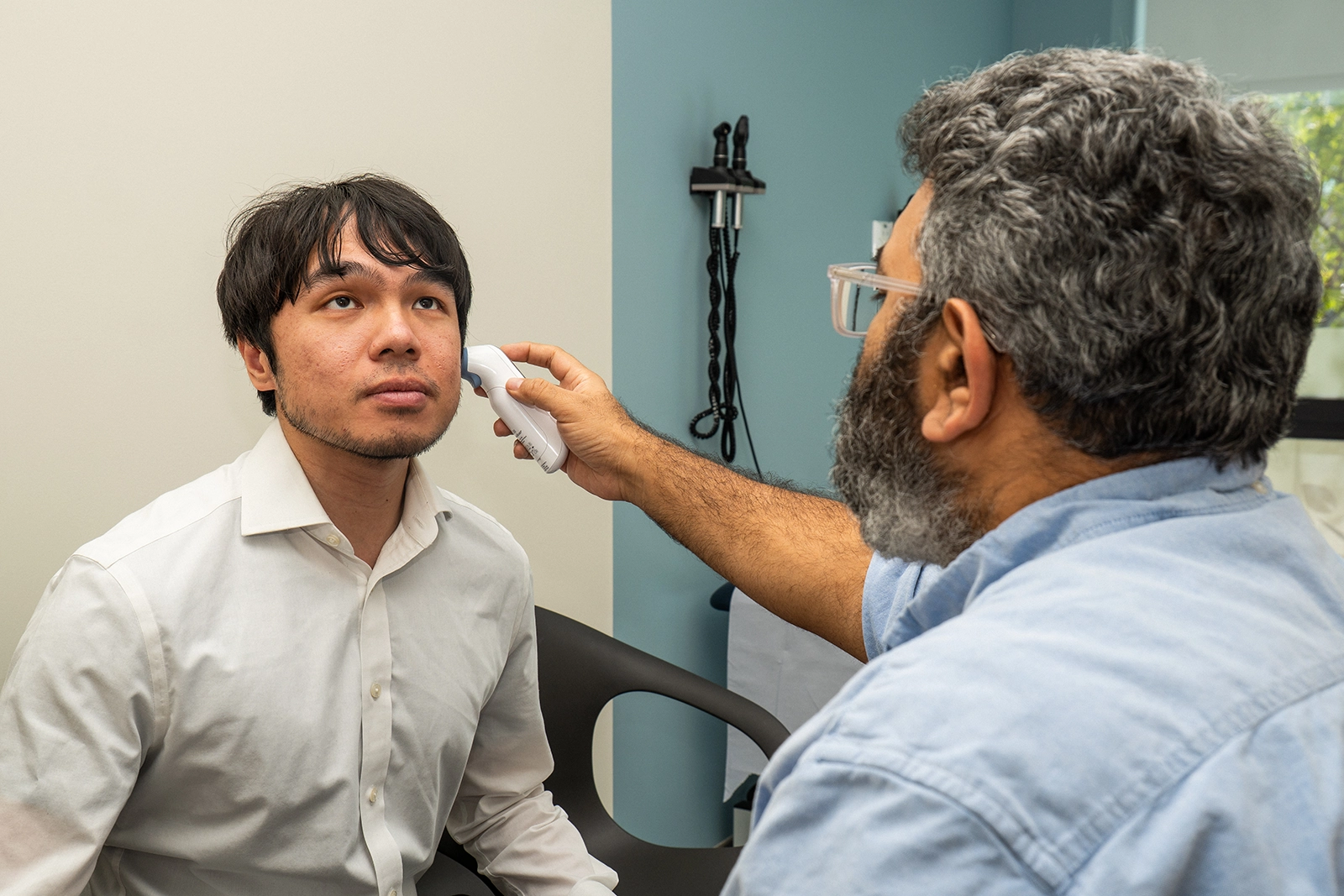 Healthcare professional using a digital ear thermometer to check the temperature of a seated male patient.
