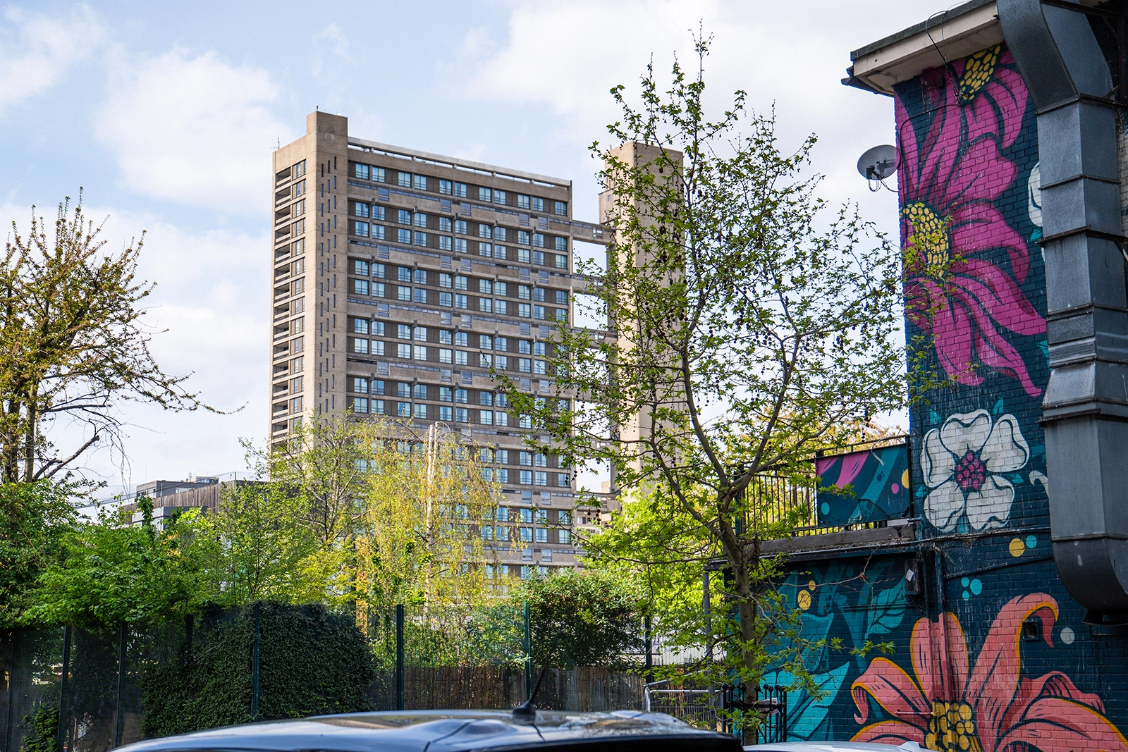 Tall residential building (balfron tower) behind trees with a colorful floral mural painted on a nearby wall.