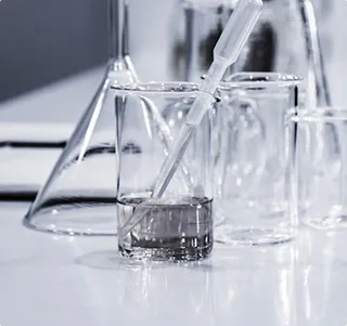 Lab glassware including a beaker with liquid and a pipette, and a conical flask blurred in background on a white surface.