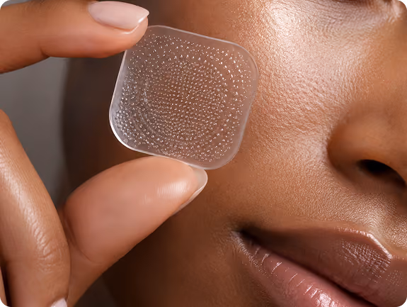 Close-up of fingers holding a clear adhesive patch near a smiling cheek.