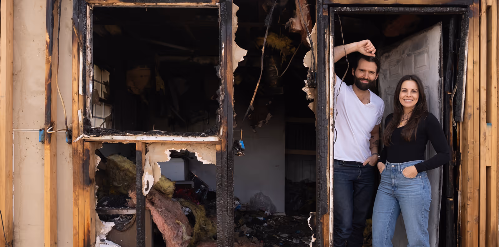Coco and Cash standing together in the doorway of a severely fire-damaged house.