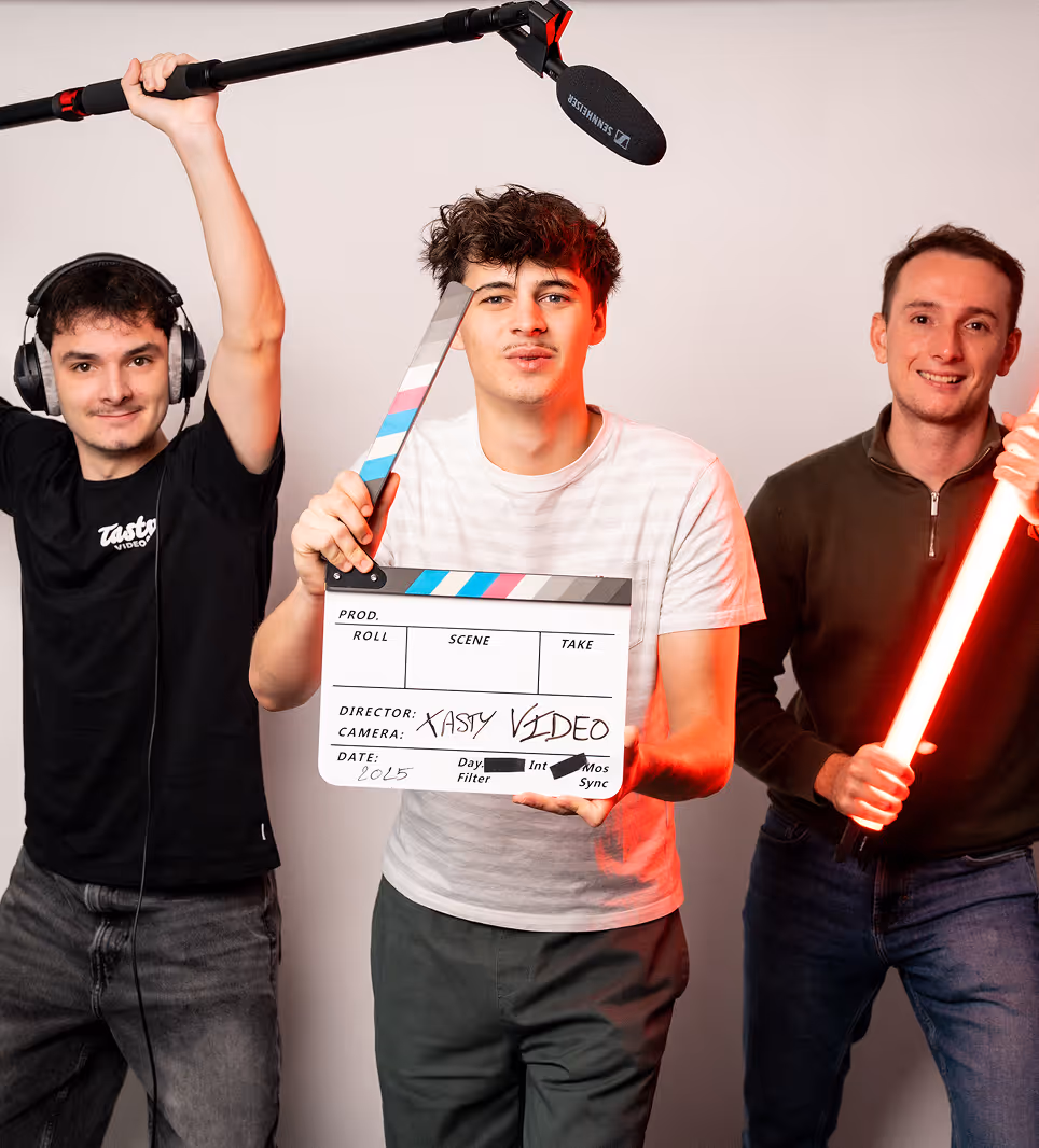 Trois jeunes hommes en studio vidéo, l'un tient une clapperboard, un autre une perche micro, et le troisième une lumière LED rouge.