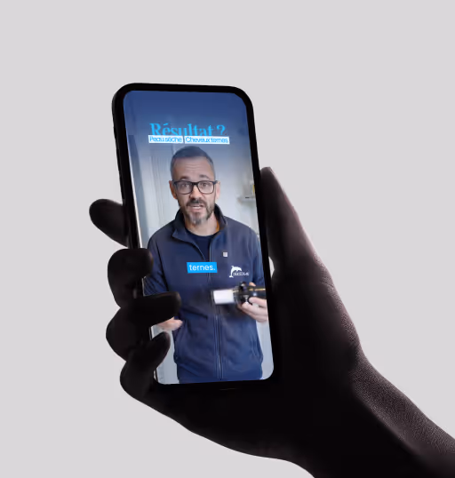 Main tenant un smartphone montrant un homme avec des lunettes expliquant des soins pour peau sèche et cheveux ternes.