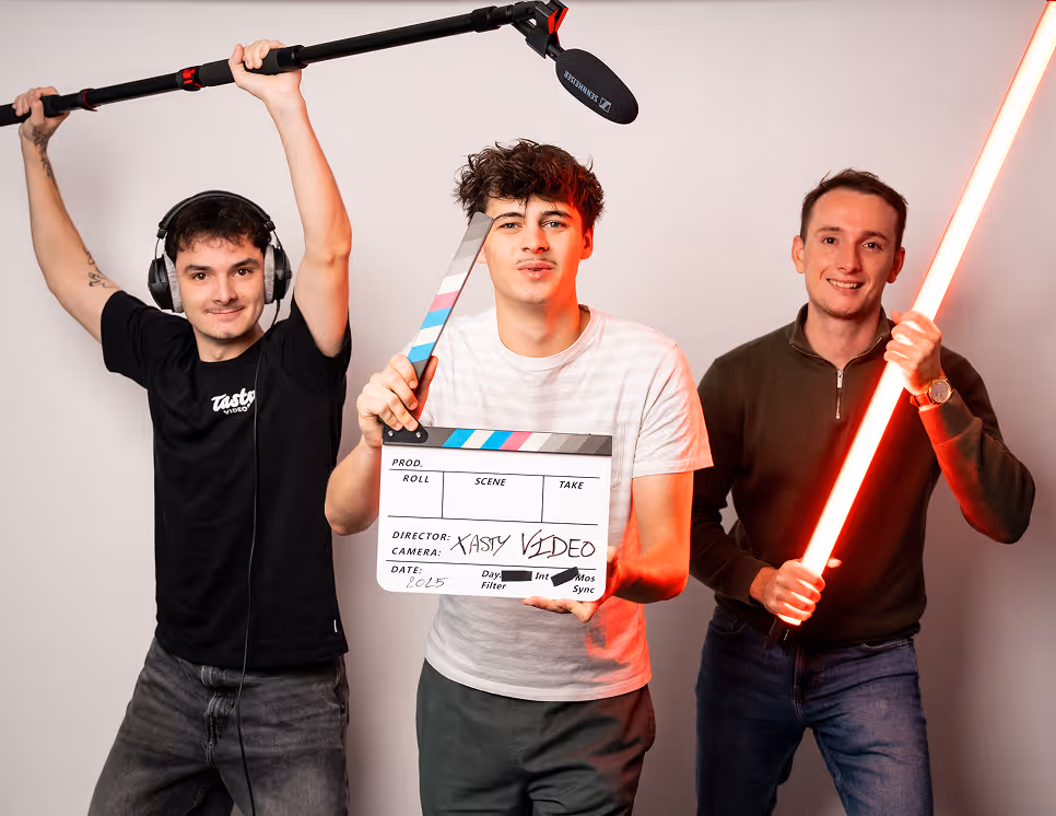 Trois jeunes hommes en studio, l'un tient une perche avec microphone, un autre une claquette de cinéma, et le troisième une lumière rouge allumée.